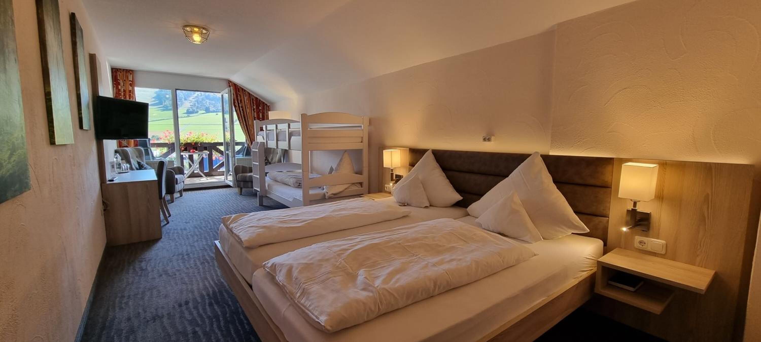 Ein Hotelzimmer mit zwei Betten, einem Fernseher, einem Schreibtisch und einem Balkon mit Bergblick.
