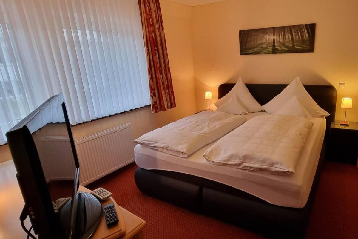 A hotel room with a bed, a TV, a chair, and a painting on the wall.