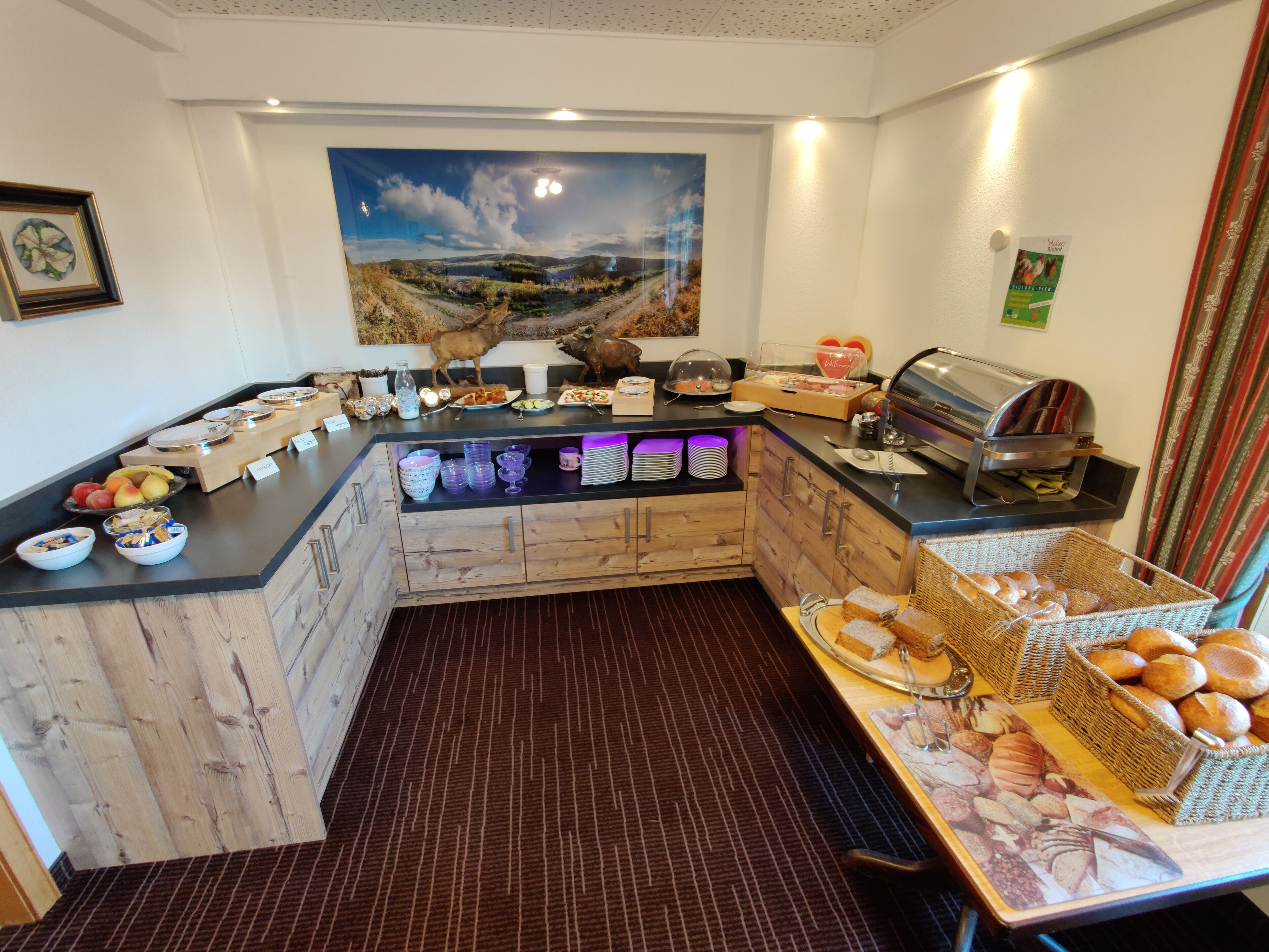 Disposición de bufé con diferentes opciones de comida, una máquina de café y un cuadro decorativo en la pared.