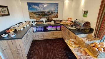 Disposición de bufé con diferentes opciones de comida, una máquina de café y un cuadro decorativo en la pared.
