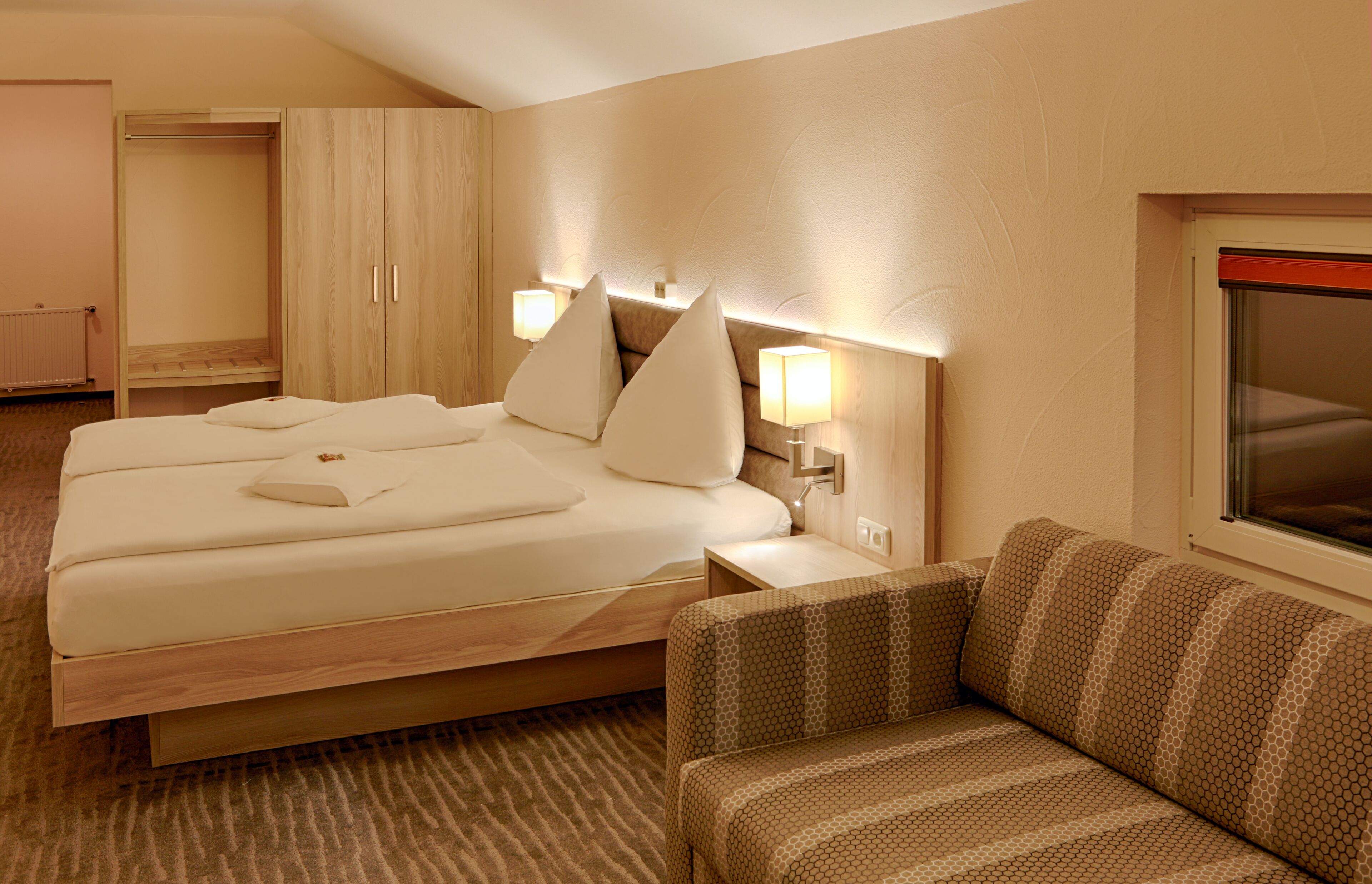 Ein Hotelzimmer mit Bett, Sofa, Kleiderschrank und Fenster.