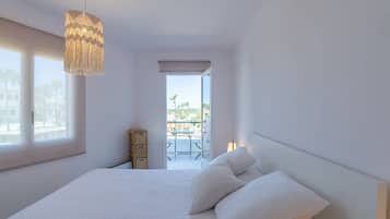 A bedroom with a large bed, a hanging light fixture, a view of the balcony, and a window.