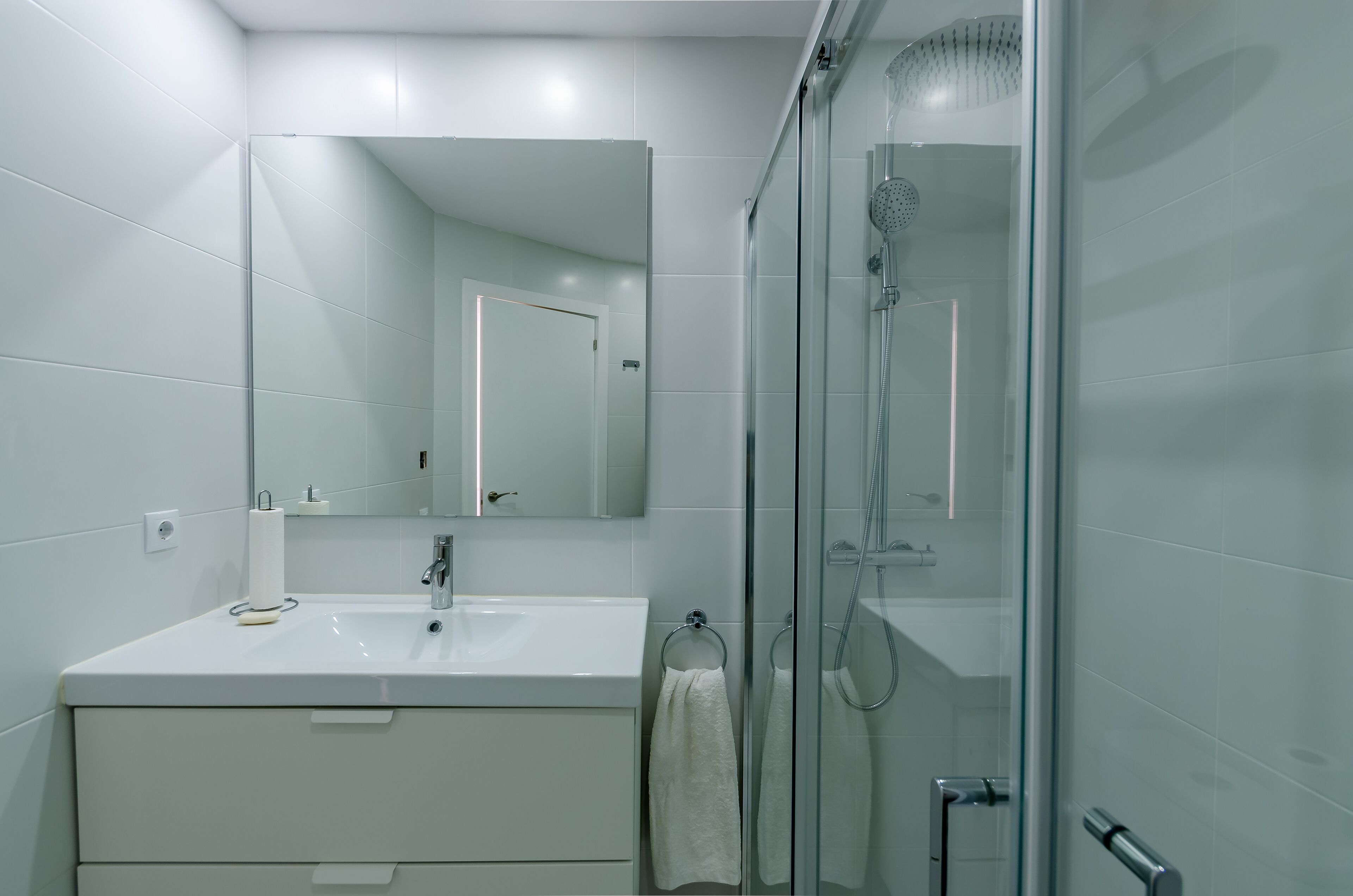 A modern bathroom with a glass shower enclosure, a white sink, and a large mirror.