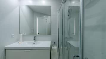 A modern bathroom with a glass shower enclosure, a white sink, and a large mirror.