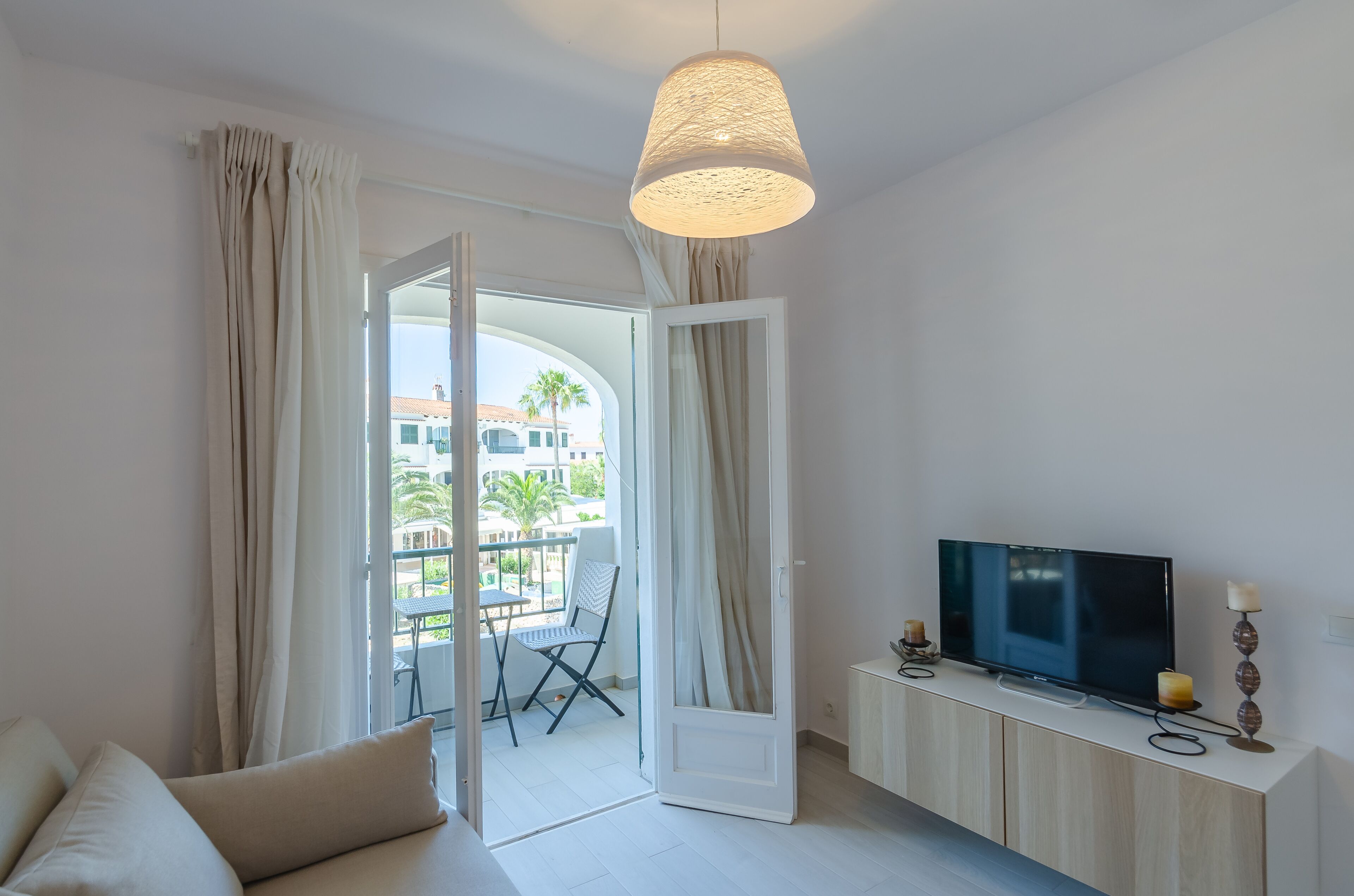 A modern living room with a sofa, TV, and a balcony with a table and chair.