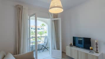 A modern living room with a sofa, TV, and a balcony with a table and chair.