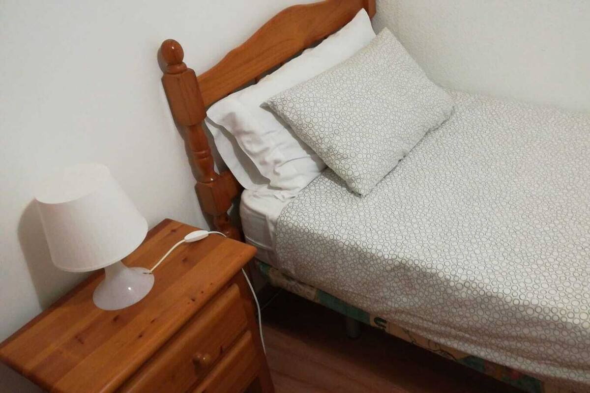 Una cama individual con una colcha estampada y almohadas, una mesita de noche de madera con una lámpara y un cabecero de madera.