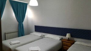 Ein Hotelzimmer mit zwei Betten, einem blauen Kopfteil, einem Nachttisch mit Lampe und einem Fenster mit Vorhängen.