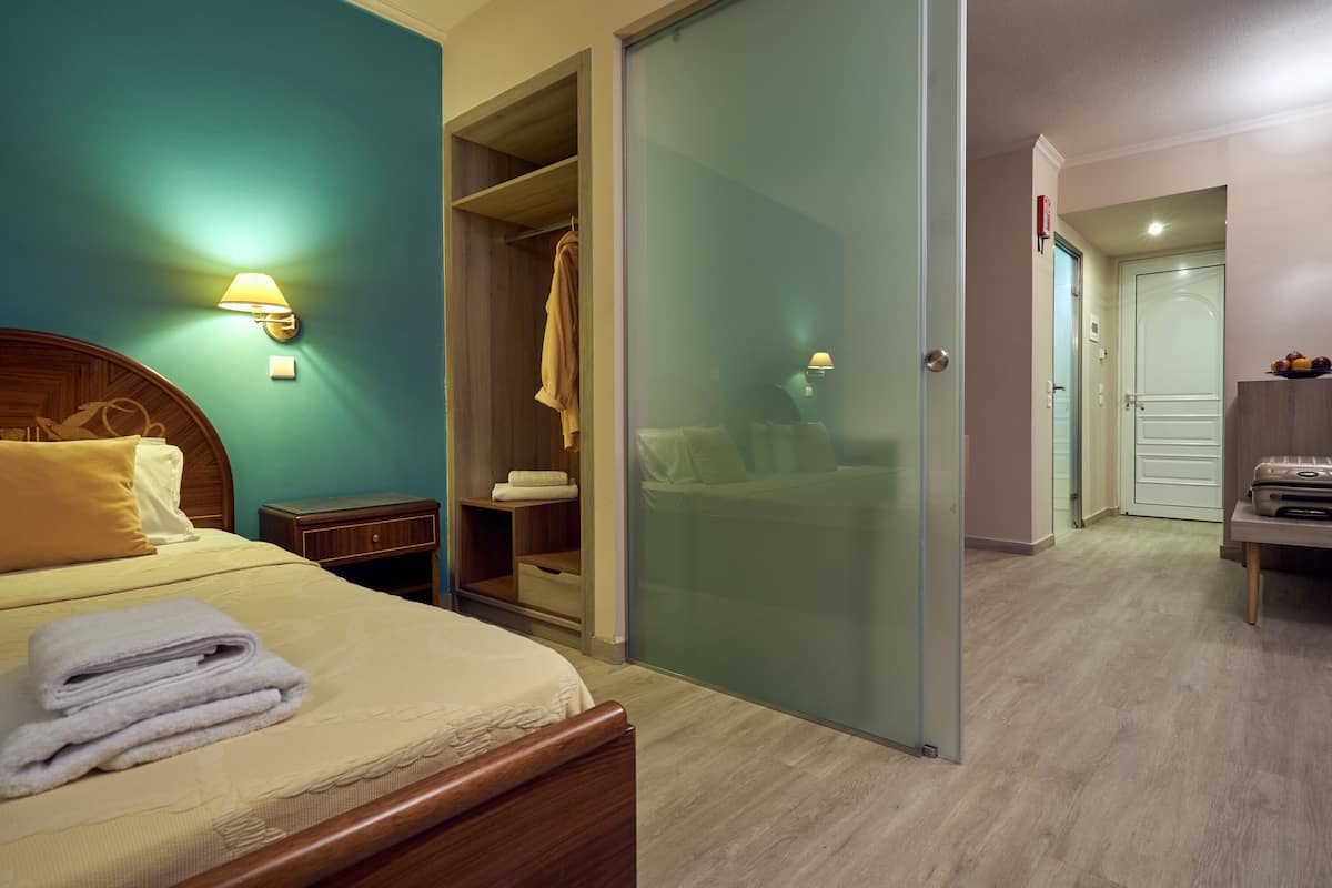 A hotel room with a bed, a nightstand, a wardrobe, and a bathroom visible through a glass door.