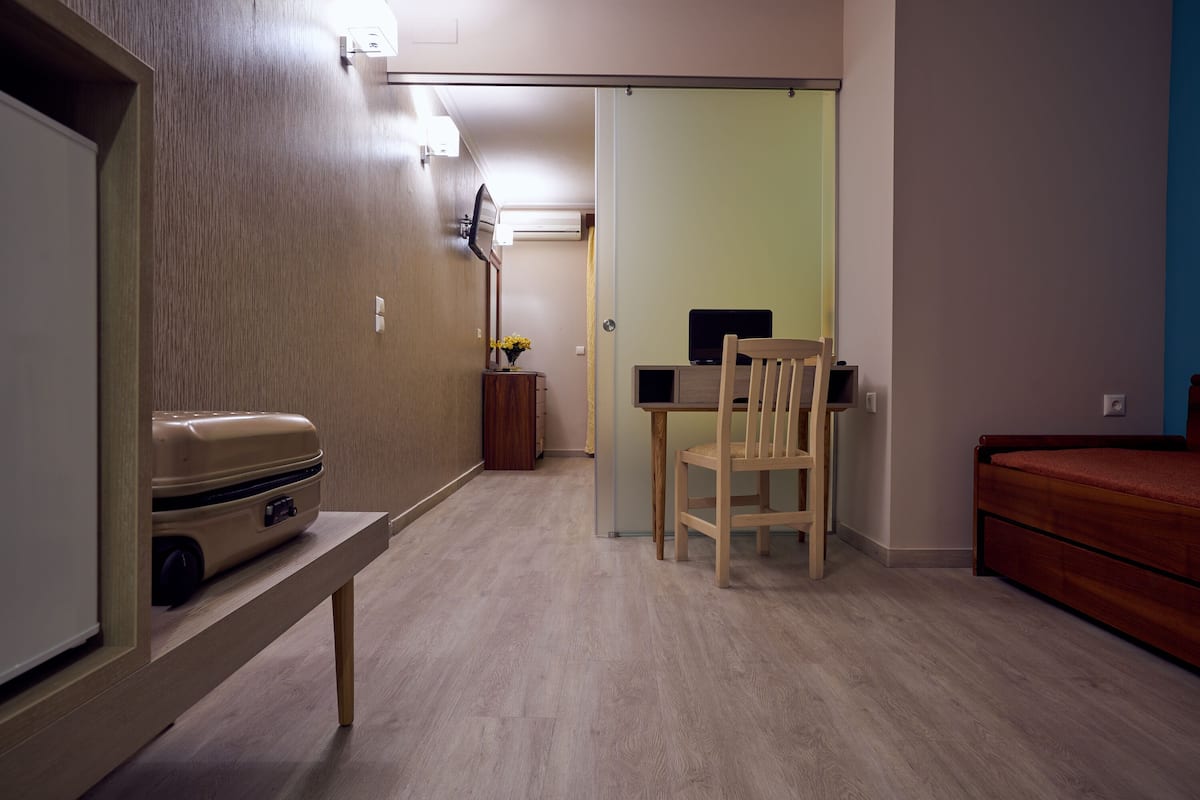 A room with a bed, a desk with a chair, a small table with a suitcase, and a mirror on the wall.