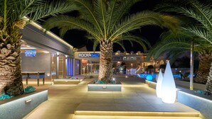 A well-lit outdoor area with palm trees, a pool, and a building with a 'Rock Salt' sign. - Ionion Blue Hotel (Zakynthos)