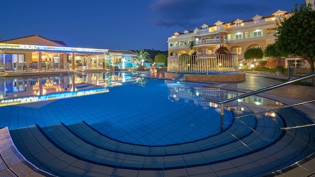 A swimming pool with a tiled deck, a restaurant named "Rockstar" in the background, and a multi-story building with balconies. - Ionion Blue Hotel (Zakynthos)