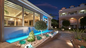 A modern hotel with a pool area, large windows, and a well-lit exterior. - Ionion Blue Hotel (Zakynthos)