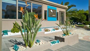 A modern building with a sign reading "Rock Salt Restaurant." It features large windows, a tiled patio, and various plants. - Ionion Blue Hotel (Zakynthos)