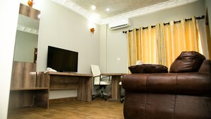 Una sala de estar con un sofá de cuero marrón, un escritorio de madera con una computadora, un televisor de pantalla plana y un aire acondicionado instalado en la pared.