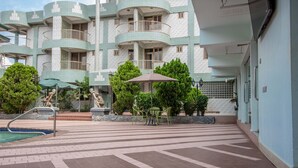 Un patio de hotel con piscina, mobiliario exterior y una estatua.