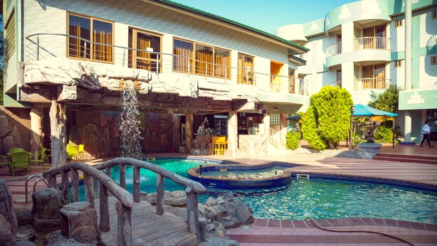 Hotel con zona de piscina que incluye una cascada, un puente de piedra y sillas de descanso.