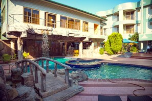 A hotel with a pool area featuring a waterfall, stone bridge, and lounge chairs. - Ange Hill Hotel (Accra)