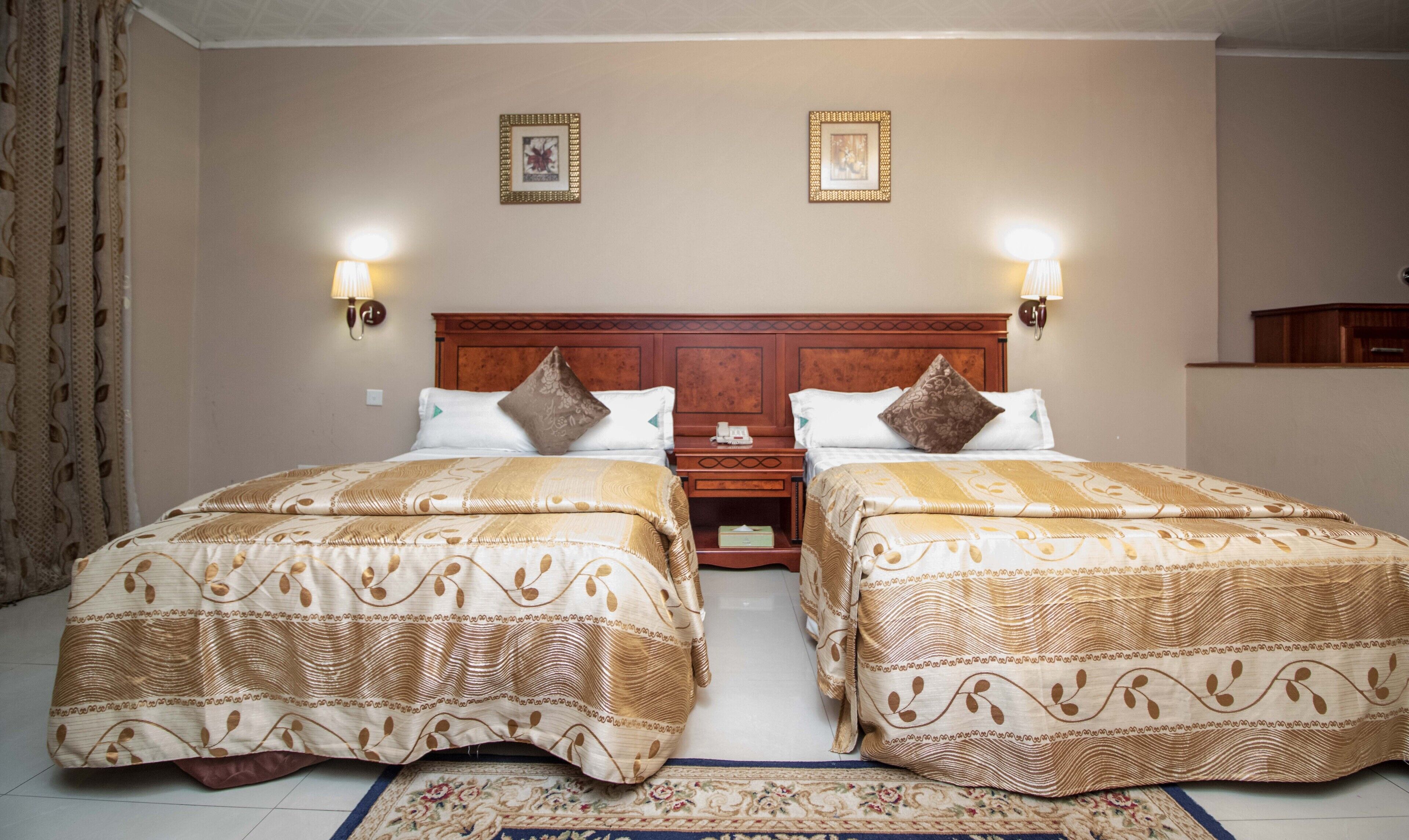A hotel room with two beds, each with a patterned bedspread, a wooden headboard, and wall-mounted lamps.