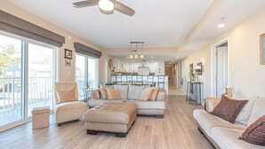 A spacious living room with a large sectional sofa, a chaise lounge, and a dining area in the background. - Upscale, stylish 3 bedroom condo with free WiFi, and outdoor pool, and a breathtaking view of the bay located in midtown and only two blocks from the beach! (Ocean City)
