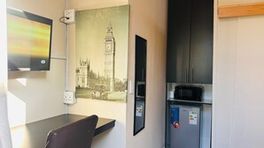 A compact room with a dining table, a chair, a refrigerator, and a microwave. A vintage photograph of Big Ben is mounted on the wall. - Karibu Guesthouse (Cape Town)