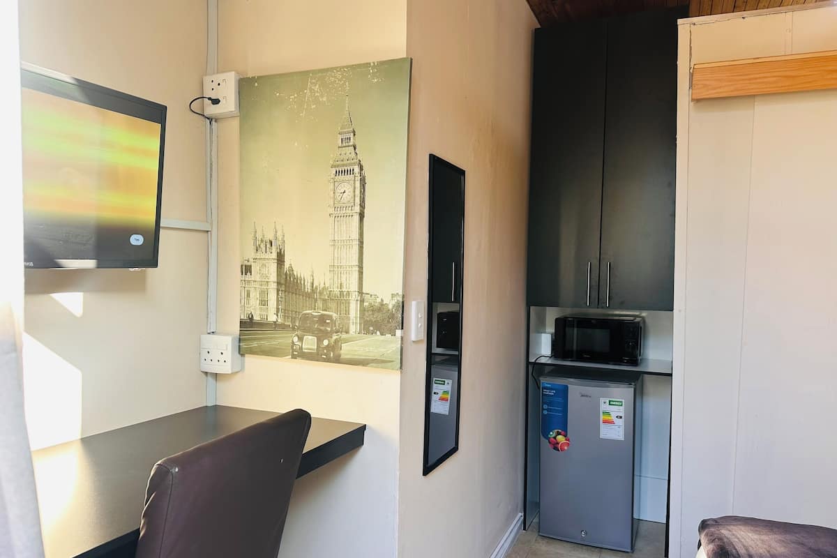 A compact room with a dining table, a chair, a refrigerator, and a microwave. A vintage photograph of Big Ben is mounted on the wall.