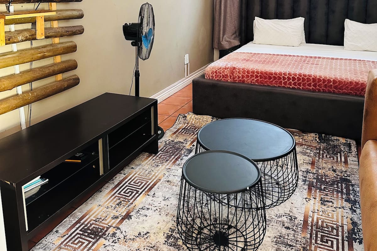 A modern hotel room with a large bed, a TV mounted on a wooden panel, a small table, and a patterned rug.