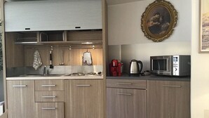 Een kleine keuken met houten kastjes, een inbouwoven, een magnetron en een waterkoker.