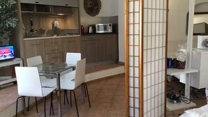 Een moderne keuken met houten kastjes, een magnetron en een eethoek met een glazen tafel en witte stoelen.
