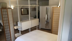 Een slaapkamer met een bed, een witte kledingkast, een badkamer met een spiegel en een toilet.