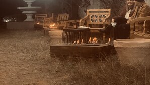 Un área de estar al aire libre con un pozo de fuego, sillas de madera y una fuente al fondo.