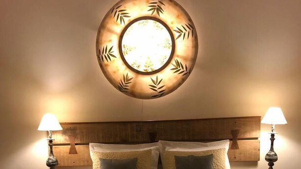 Una cama bien hecha con cabecera, dos mesitas de noche con lámparas y una lámpara de pared.