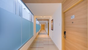 Un pasillo moderno de hotel con una puerta de madera con la etiqueta "604" y una ventana con marco azul a la izquierda.