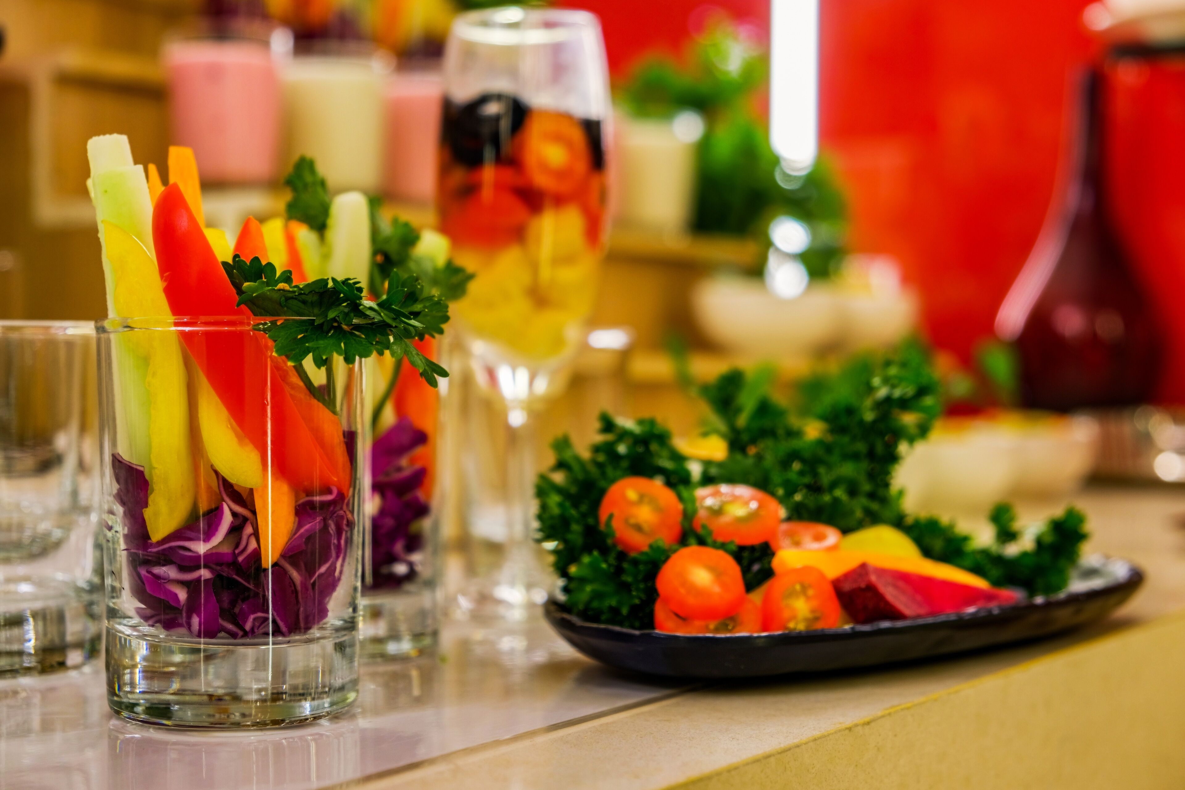 A glass with a colorful fruit and vegetable garnish, a plate of fresh vegetables, and a glass of beverage.