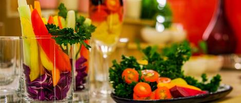 A glass with a colorful fruit and vegetable garnish, a plate of fresh vegetables, and a glass of beverage.