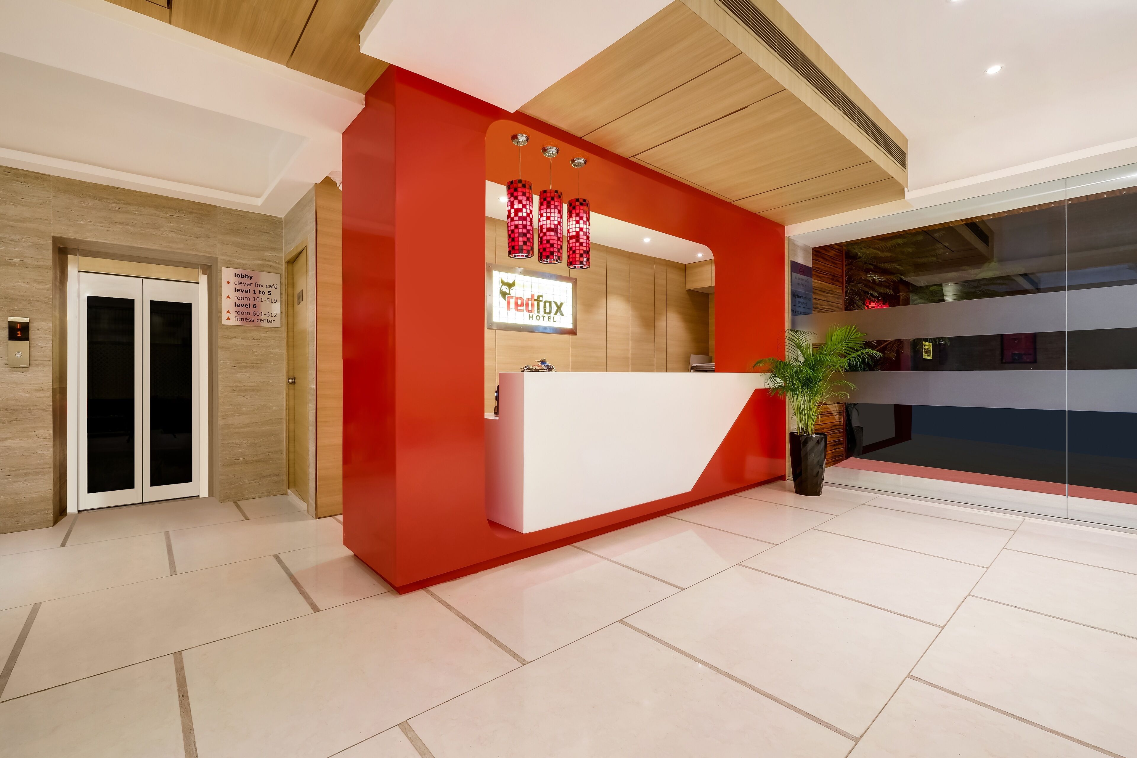 Een hotel receptiebalie met een rood-wit kleurenschema, een digitaal scherm en een kamerplant.