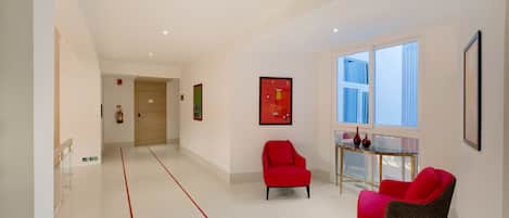 A modern hotel lobby with a clear floor layout, a seating area with red chairs, and a glass table with decorative items.