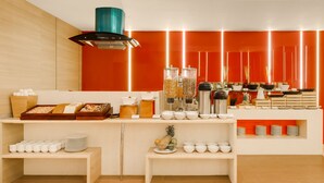 Una barra de desayuno moderna con diversos alimentos y utensilios, como cuencos, platos y una cesta de frutas.