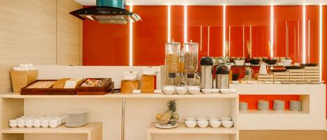 A modern breakfast bar with a variety of food items and utensils, including bowls, plates, and a fruit basket.