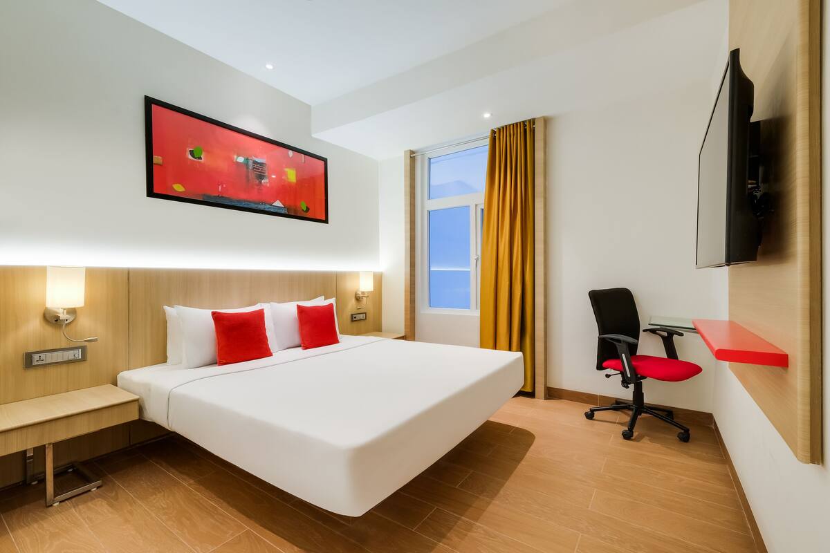Une chambre d’hôtel moderne avec un grand lit, un bureau, une chaise, une télévision et une fenêtre avec des rideaux.