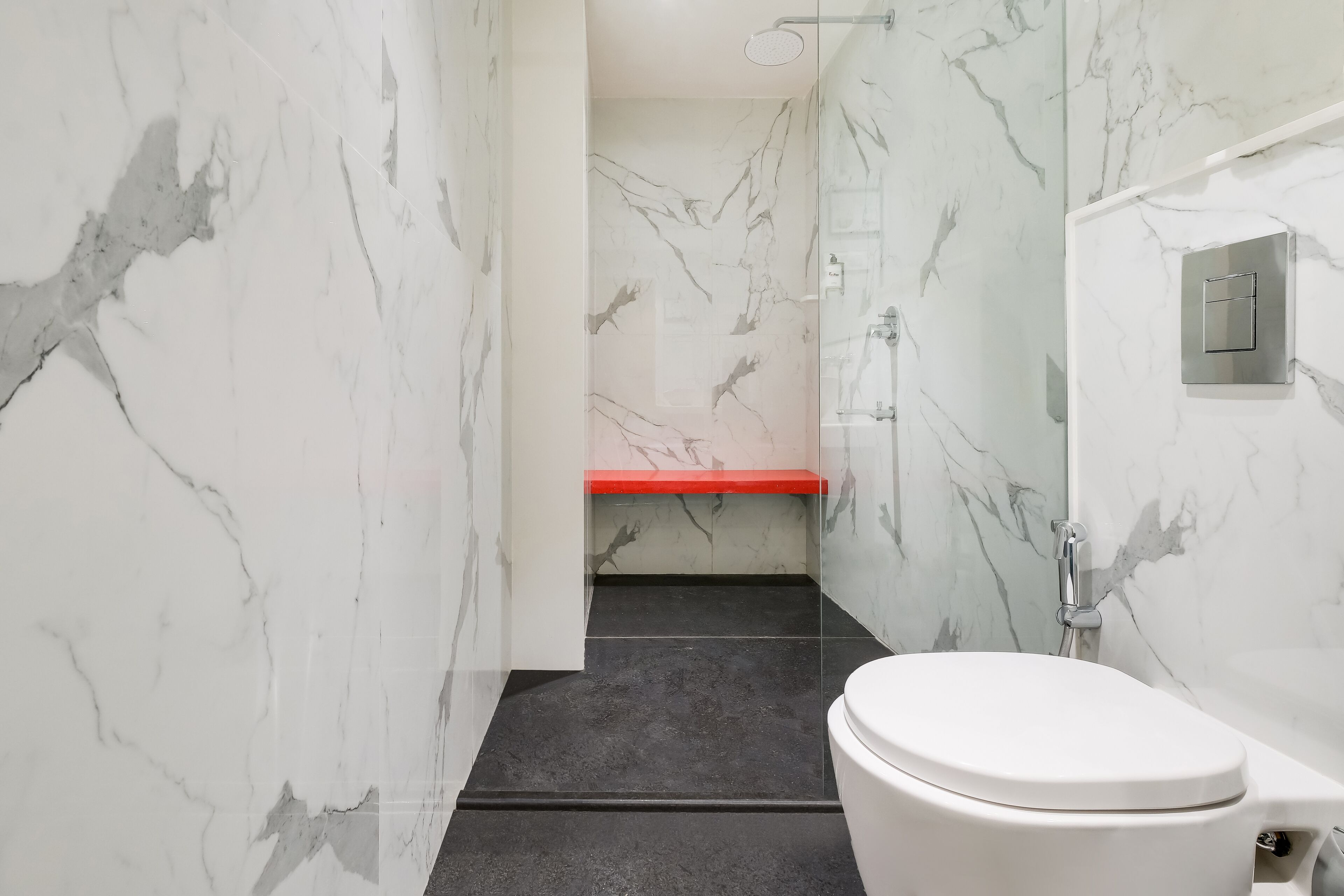 A modern bathroom with a white toilet, a shower area, and a marble wall.