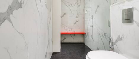 A modern bathroom with a white toilet, a shower area, and a marble wall.