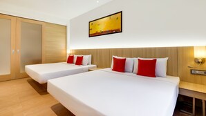 Una habitación de hotel con dos camas, cabeceros de madera, ropa de cama blanca, almohadas rojas, un cuadro en la pared y suelo de madera.