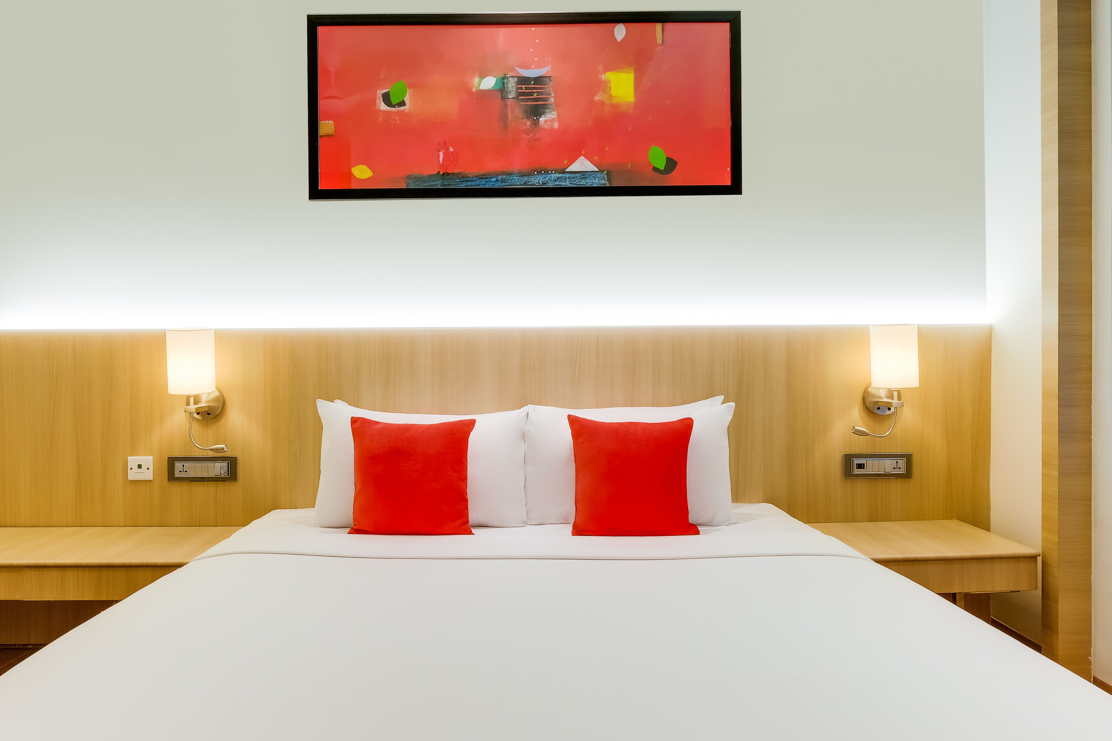 Une chambre d’hôtel avec un grand lit, deux tables de chevet, un téléviseur fixé au mur et deux lampes fixées au mur.