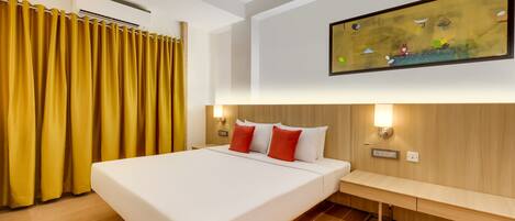 A hotel room with a large bed, yellow curtains, a ceiling fan, a wall-mounted light, and a painting.
