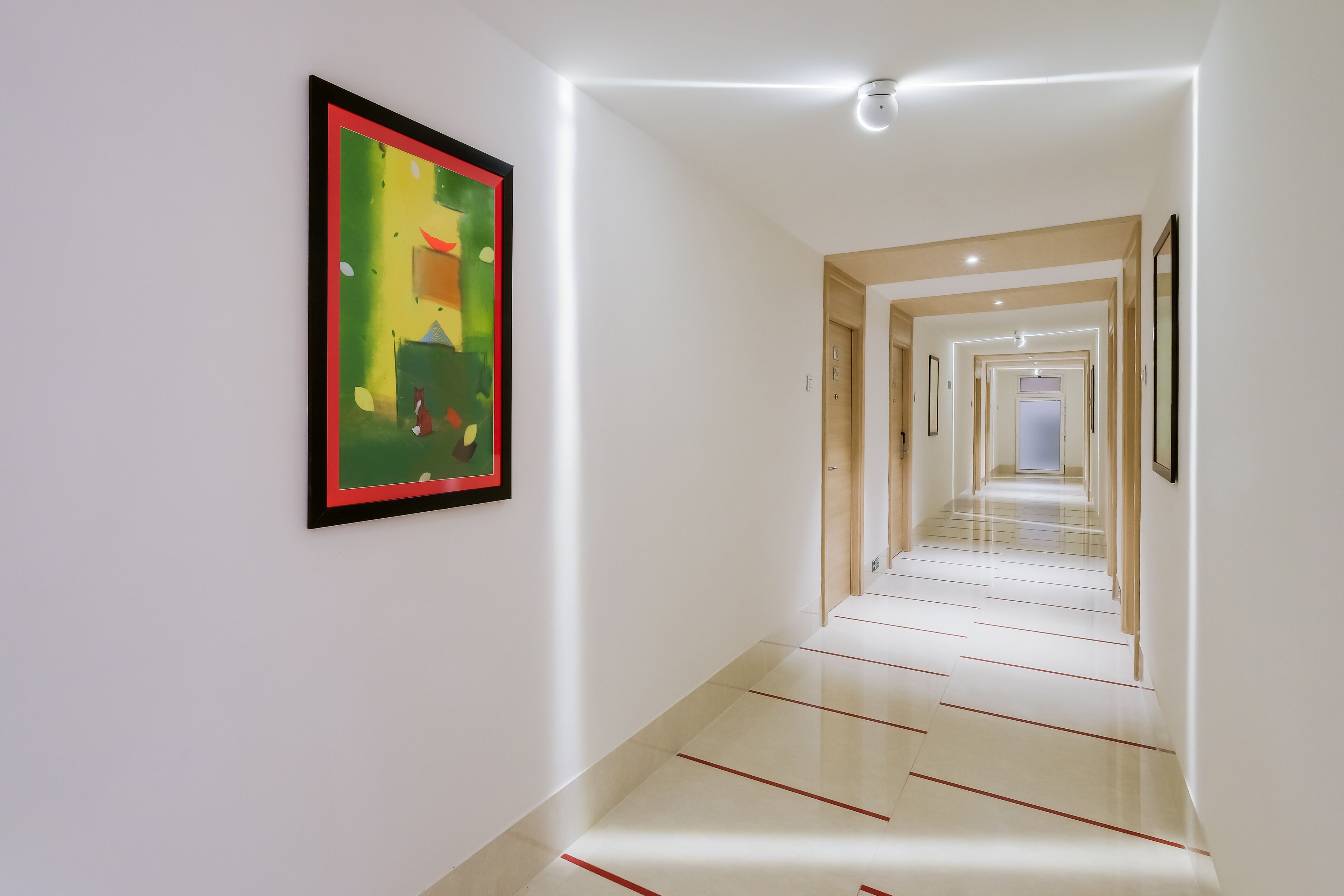 A modern, well-lit hallway with a framed abstract painting on the wall, leading to a series of doors.