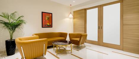 A modern living room with a sofa, armchair, and coffee table. There is a potted plant and a framed picture on the wall.