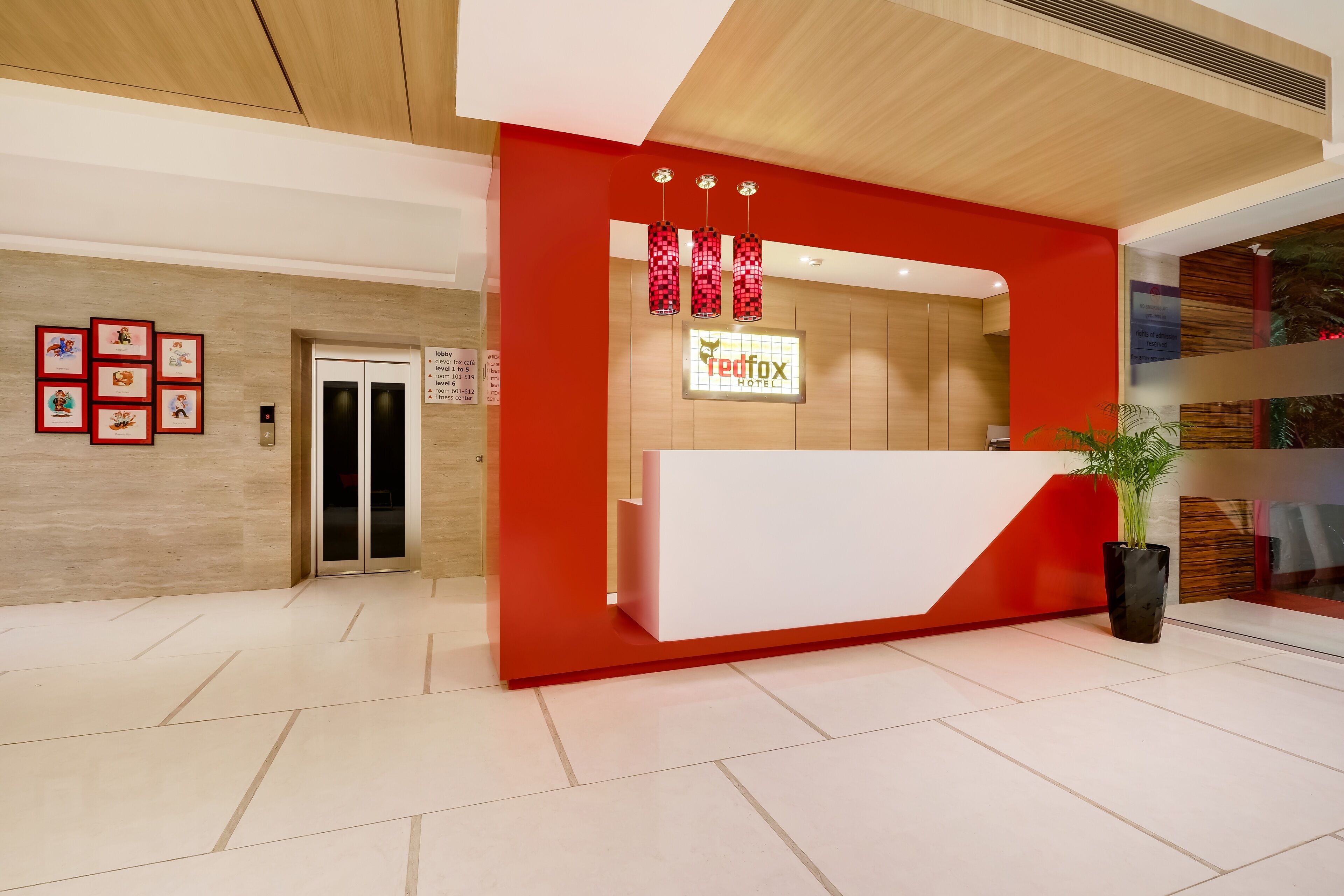 A hotel reception area with a modern design, featuring a red and white color scheme, a reception desk, and a digital elevator display.