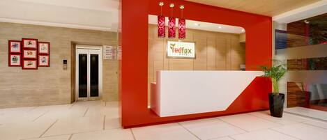 A hotel reception area with a modern design, featuring a red and white color scheme, a reception desk, and a digital elevator display.