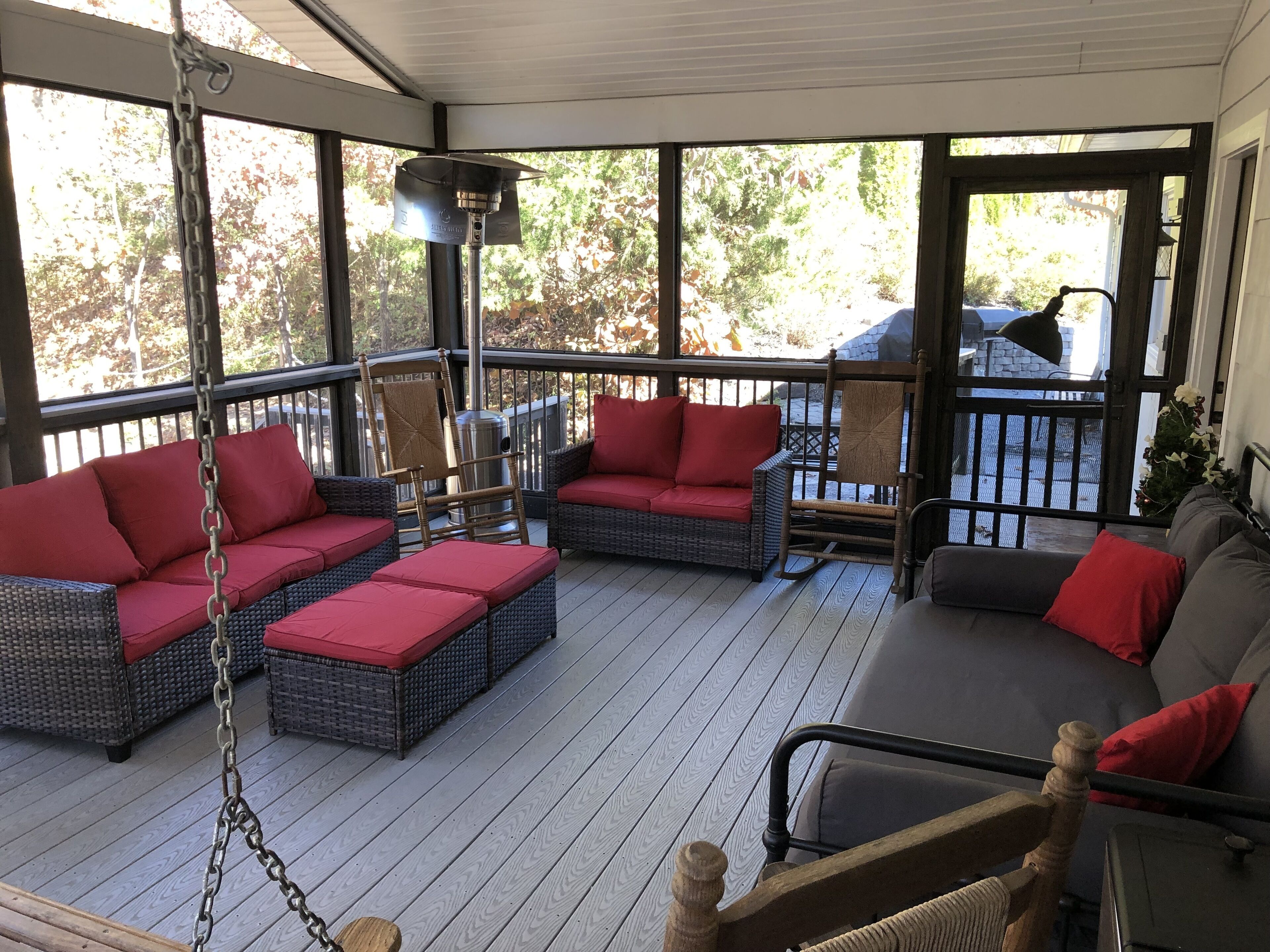 A covered porch with wicker furniture, red cushions, and a metal heater.